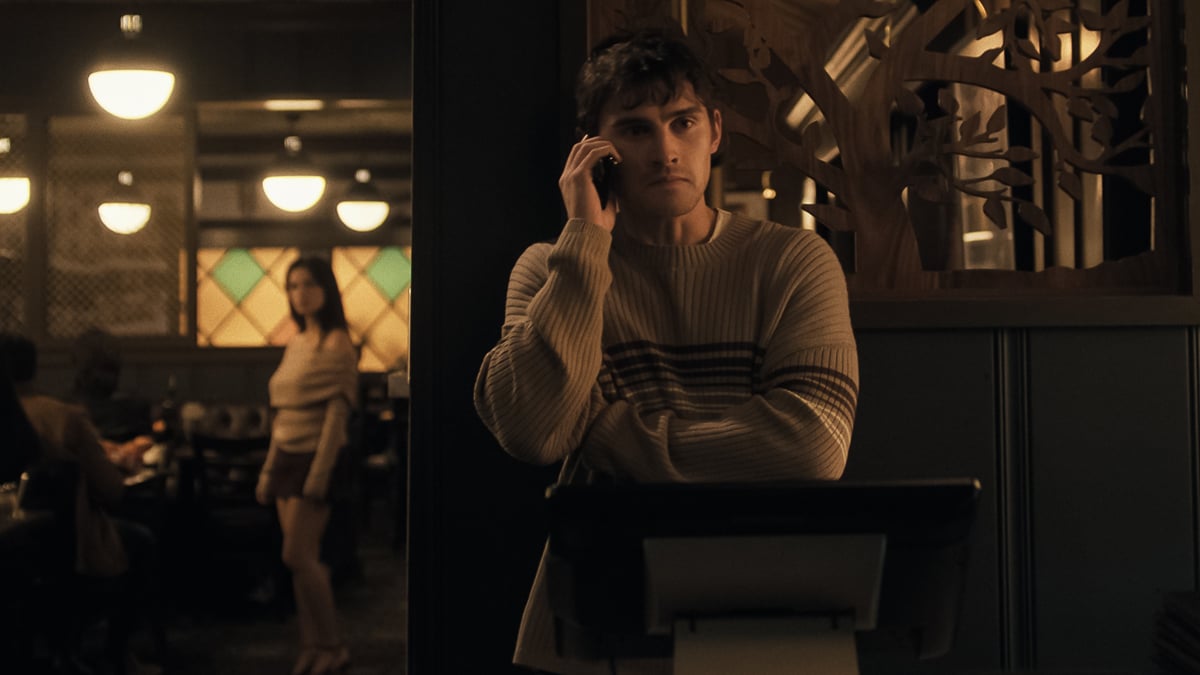 Still from "Obsession" — the main character on the phone in a dimly-lit café